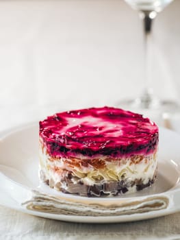 Layered salad herring under fur coat on table. Portion of traditional russian salad with herring, beet and other vegetables on white linen tablecloth. Copy space. Vertical.