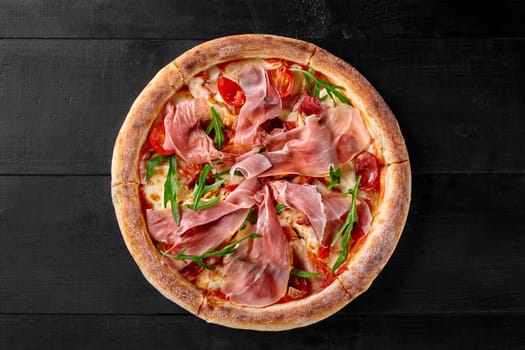 Delicious pizza with salami, chicken fillet and thin slices of Italian prosciutto on base with pelati sauce and mozzarella cheese garnished with fresh tomatoes and arugula leaves on black background