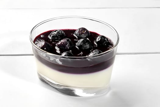 Light flavorful creamy panna cotta topped with blueberries and lavender coulis served in glass on white wooden background. Italian dessert. Natural organic sweets