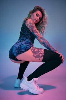 Beautiful young blonde tattoed girl in blue velour booty shorts and t-shirt and black stockings, making squats , showing off her amazing booty