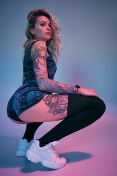 Beautiful young blonde tattoed girl in blue velour booty shorts and t-shirt and black stockings, making squats , showing off her amazing booty