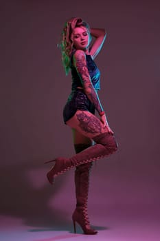 Young beautiful tattooed blonde woman wearing blue velour booty shorts and t-short, maroon suede boots showing her amazing body in studio.