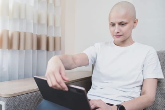 Young bald woman looks at laptop at home, sick leave.