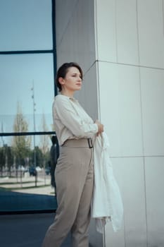 Successful business woman in stylish beige pant suit standing near office building and confidently looks to the future, copy space, vertical.