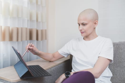 Young bald woman looks at laptop at home, distance learning or remote work, sick leave.