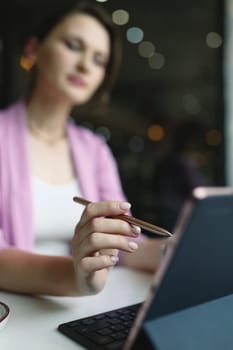 Stylus from a tablet in a woman's hand in front of a tablet on a table in cafe, freelance work concept, vertical.