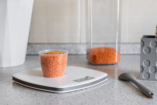 Kitchen scale with measuring cup with red lentils on the kitchen desktop. Concept of a healthy diet or diet for weight loss.
