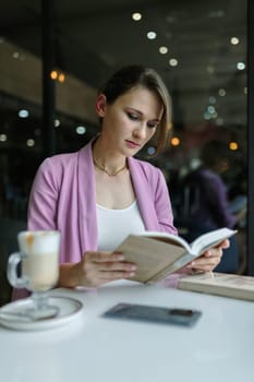 Young cute caucasian woman reading a book in a cafe, copy space, vertical.