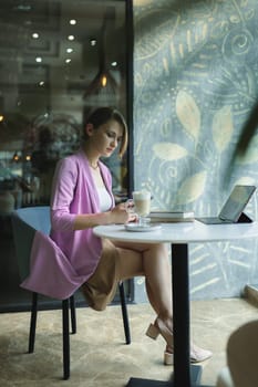 Business woman sitting in cafe with coffee, books and laptop. Remote working in a cafe, vertical.