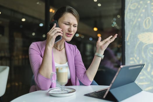 Upset young business woman emotionally talking on the phone in a cafe.