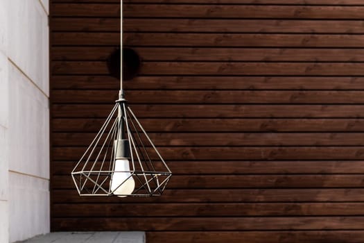 Modern garden pendant lamp hanging on the outdoor terrace during on wooden wall background.
