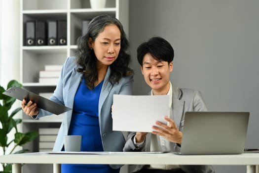 Professional senior female manager explaining information, discussing business plan with young businessman.