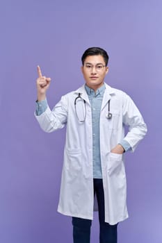 Male doctor makes a pointing finger gesture, isolated over a purple background