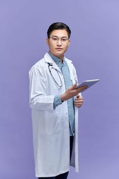 A friendly Asian male doctor in a white coat and black stethoscope using a tablet computer,