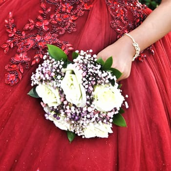 Hand of the bride girl with a wedding bouquet of white and pink flowers on a red dress. High quality photo