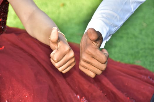 hands of newlyweds with like symbol from fingers, bride in red on green grass. High quality photo