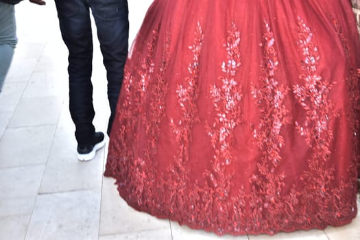 The hem of the lush red wedding dress of the bride and the legs of the boyfriend of the groom in black jeans, newlyweds. High quality photo