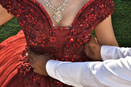 A scarlet dress is on the bride, the hands of the groom's man are holding the girl by the waist. No faces, clothing details. High quality photo