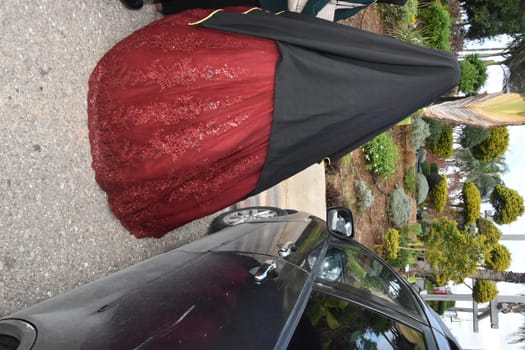 arabic girl bride in a scarlet wedding dress and black cape stands with her back on the street near a black car. High quality photo