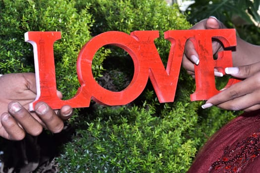 The palms of a man and a woman, hold the word Love from red letters on a green natural background. Newlyweds, lovers.Valentine's Day. High quality photo