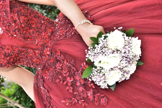 Hand of the bride girl with a wedding bouquet of white and pink flowers on a red dress. High quality photo
