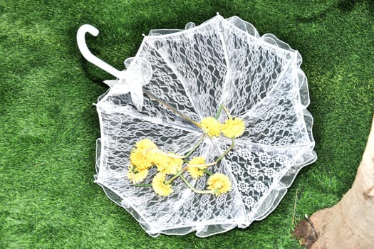 White lace wedding umbrella with yellow flowers thrown on green grass. High quality photo