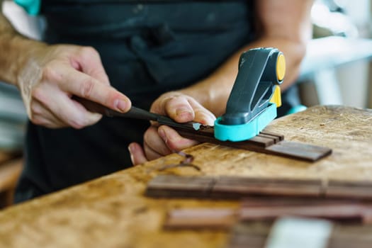 Soft focus of unrecognizable craftsman carving part for Spanish flamenco guitar on workbench during work in luthier workshop