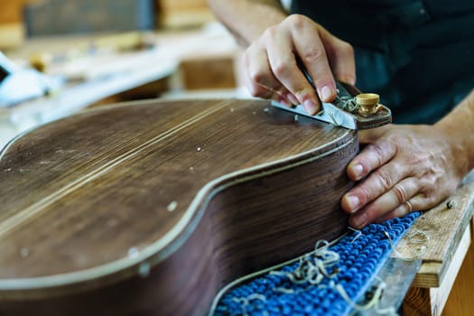 Crop craftsman using plane to shave traditional Spanish flamenco guitar on workbench in workshop