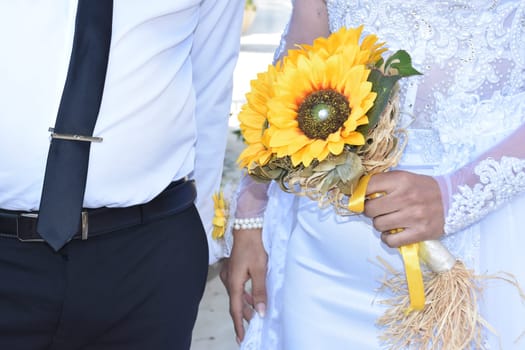 groom with black tie and bride in white with a bouquet of yellow sunflowers. High quality photo