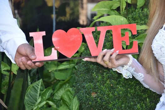the hands of the bride and groom hold the word love made of red letters. High quality photo