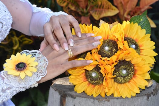 the bride's hands with gold rings lie on a bouquet of yellow sunflower flowers. High quality photo