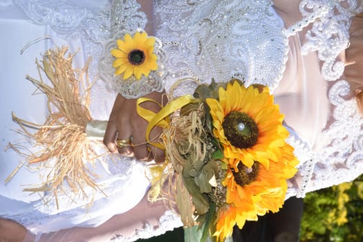 the bride's hands with gold rings are holding a bouquet of yellow sunflower flowers. High quality photo