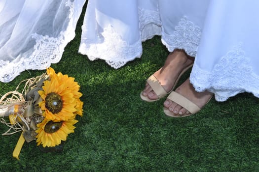 white bride dress, legs in sandals on the grass, yellow flowers. High quality photo