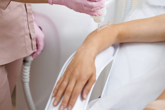 Applying a contact transparent gel before the laser hair removal procedure. Closeup of woman having hands epilation in beauty salon. Skin care, cosmetic procedures.