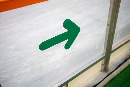 Green arrow sign on fence near ice skate rink