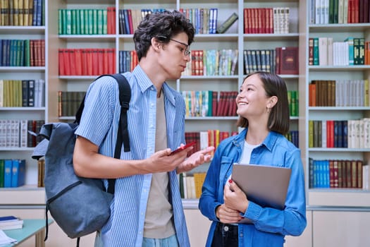 Cheerful talking college students male and female with books backpacks meeting inside library. Friendship, communication, knowledge, education, university college youth concept