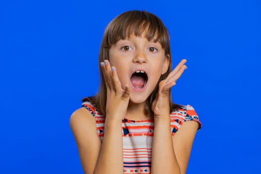Oh my God, Wow. Young preteen child girl kid looking surprised at camera with big eyes, shocked by sudden victory game winning lottery goal achievemen good news. Children isolated on blue background