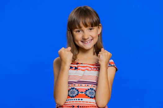 Young preteen child girl kid shouting, raising fists in gesture I did it, celebrating success, winning, birthday, lottery jackpot goal achievemen. Little cute children isolated on blue background
