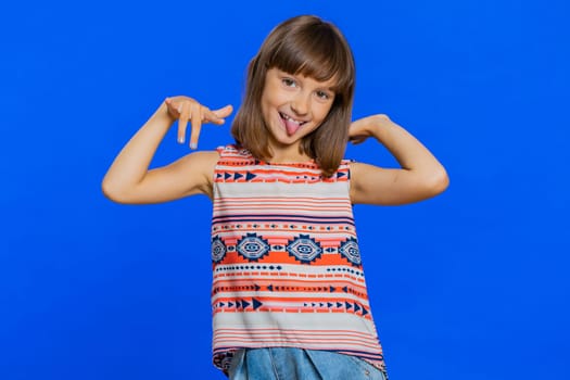 Cheerful funny bully young cute girl showing tongue making faces at camera, fooling around, joking, aping with silly face, teasing. Preteen brunette child kid on blue background. Little children