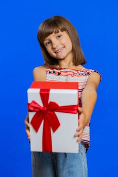 Lovely smiling preteen child girl kid presenting birthday gift box stretches out hands, offer wrapped present career bonus, celebrating party. Little cute children on studio blue background. Vertical