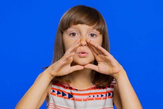 Keep my secrets, silence. Young school girl whisper news rumors holding hands near mouth share gossip quiet. Preteen child kid telling interesting confidential story isolated on studio blue background