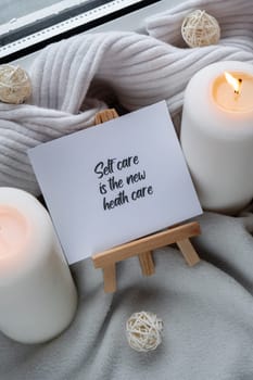 SELF CARE IS THE NEW HEALTH CARE text saying phrase on paper note on background of Home fragnance concept autumn holidays at cozy home. Still life of micro moment candid slow living. Mental health wellbeing exercises Raining Outside Hygge aesthetic atmosphere on knitted white sweater