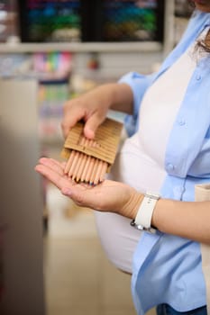 Selective focus on stylish wooden color pencils in the hands of a pregnant woman, customer, shopper shopping for school supplies in school stationery store. Drawing activity. Creative hobby. Art shop