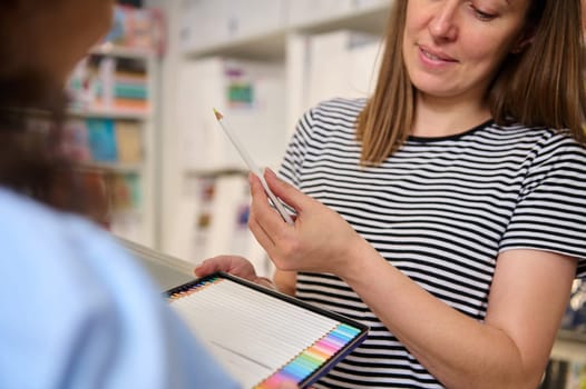 Charming female seller, sales manager, saleswoman showing color pencils of pastel spectrum to a woman customer shopping in art store. Hobby. People. Creativity. Fine art. Business and consumerism