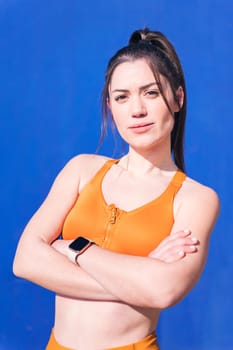 vertical close up portrait of a confident caucasian sportswoman with arms crossed in a blue background, concept of real people and sporty lifestyle