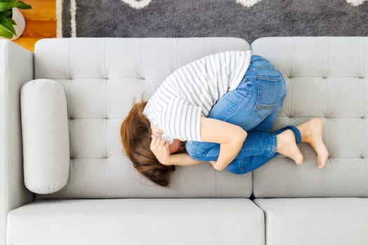 Frustrated woman covering face and crying, lying on sofa at home alone, upset female suffering from break up with boyfriend or divorce, bad relationship, feeling lonely and depressed.