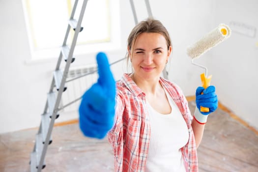 Beautiful woman with roller painter showing thumb-up while doing repair in room.