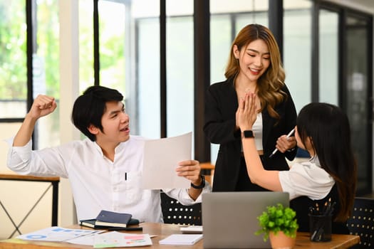 Overjoyed young employees give high five, celebrating business success or victory in office.