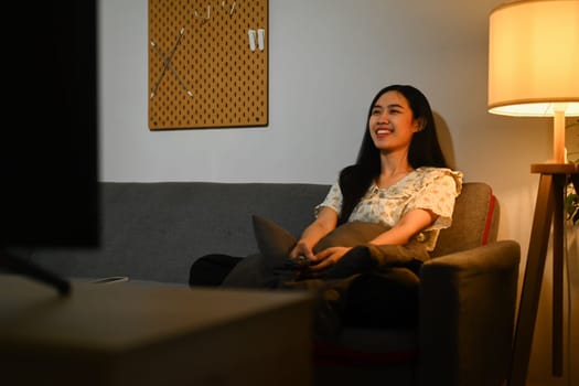 Joyful young woman watching romantic movie on TV at home in evening alone.