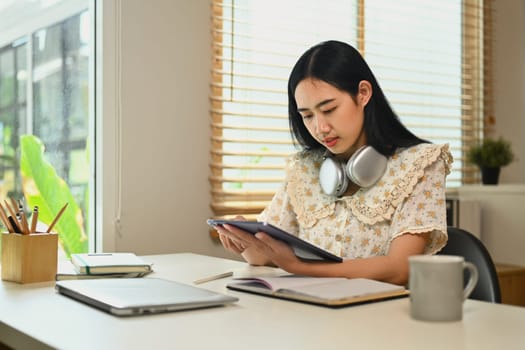 Pretty young Asian woman using digital tablet and making notes, browsing internet, remote work and stying online.